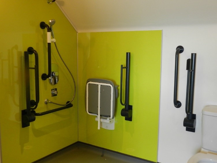 Image of accessible wet room/changing room showing shower, grab rails, toilet and shower chair.